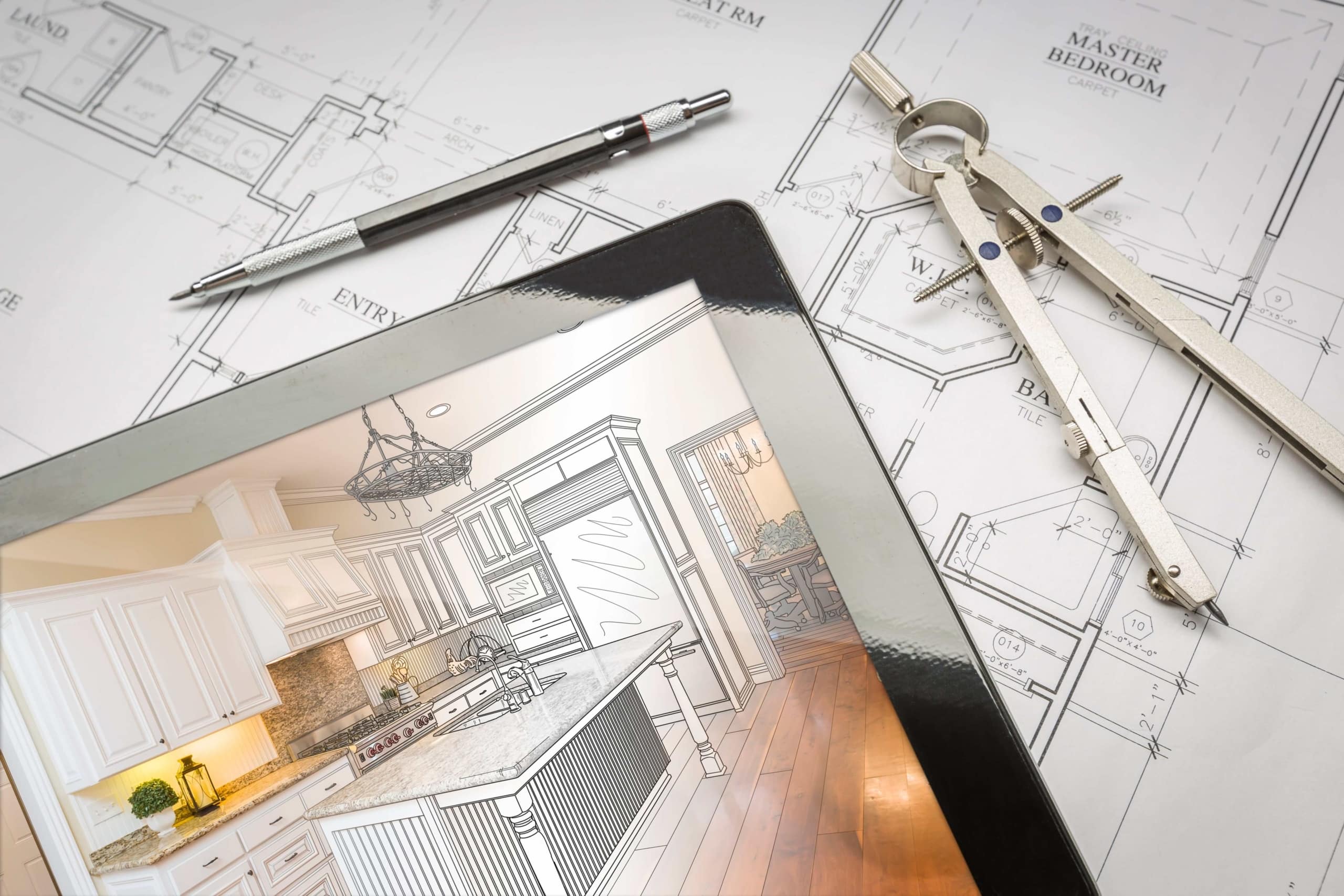 Blueprints for a home remodel with a pen, protractor, and tablet on top of it.